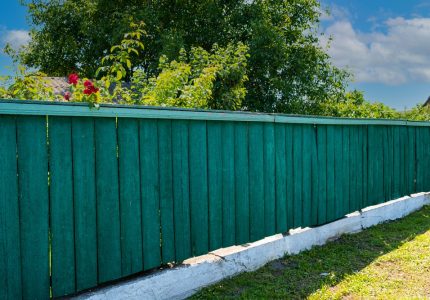 The old weathered wooden green fence near residential homes