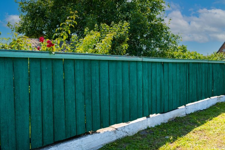 The old weathered wooden green fence near residential homes
