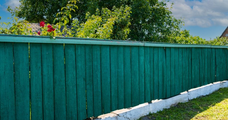 The old weathered wooden green fence near residential homes