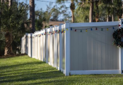 White vinyl picket fence on green lawn surrounding property grounds for backyard protection and privacy.