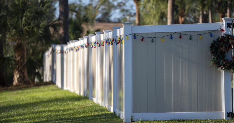 White vinyl picket fence on green lawn surrounding property grounds for backyard protection and privacy.